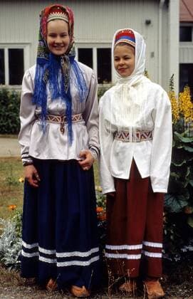 Zwei Skolt-Sami-Mädchen in traditioneller Tracht vor einem Wohnhaus im finnischen Lappland