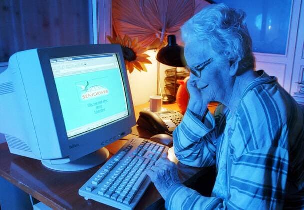 Seniorin sitzt vor einem Computer und surft im Internet