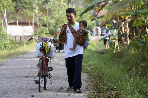Flüchtling verlässt mit einem Baby auf dem Arm und seinem Fahrrad ein Flüchtlingslager nach dem verheerenden Tsunami in Pangandaran auf Java - 