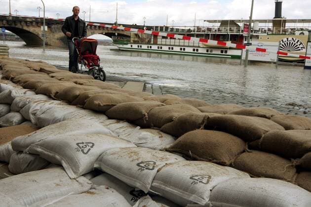 Mann mit Kinderwagen fährt vorbei an Ufer der Elbe, wo zum Schutz vor Hochwasser Sandsäcke aufgestapelt sind - Dresden