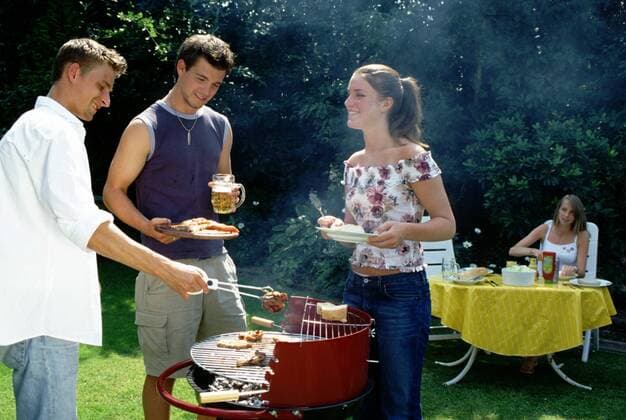 Grillparty im Sommer - Zwei junge Männer und eine Frau stehen um einen Grill