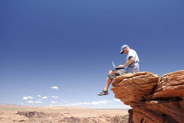 Mann sitzt mit einem Laptop auf einem Felsvorsprung am Horseshoe Bend im Bundesstaat Arizona - (ibltlf00259311)