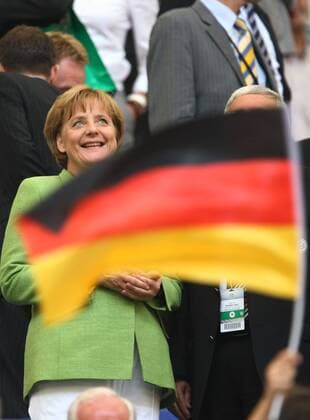 Bundeskanzlerin Angela Merkel (Deutschland CDU) hinter einer Deutschlandfahne während eines Testspiels der deutschen Fußballnationalmannschaft in Gelsenkirchen