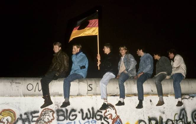 Berliner feiern ohne das ausgeschnittene Emblem aus der DDR-Fahne den Fall der Berliner Mauer rittlings auf eben jener sitzend im nächtlichen Berlin - iblnom01063073