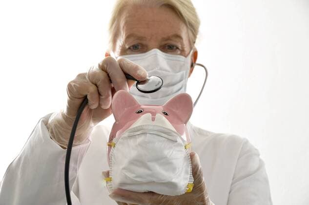 Ärztin untersucht mit Stethoskop eine Schweinefigur mit Mundschutz - MODEL RELEASED