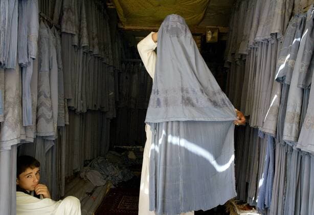 An Afghan shop keeper adjusts a burqa on a woman, which is worn to cover the entire body of women in public, as a boy looks on, in Herat, Afghanistan on August 11, 2009. The participation of women in the upcoming August 20 election is considered vital to success of those elections. UPI Mohammad Kheirkhah Daily Life in Afghanistan  AFG20090811106