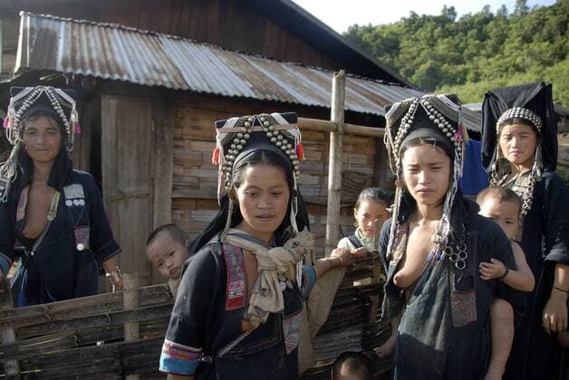 IMAGO Cultures of the world, Akha Volk in Laos Armut, Frauen der Akha Nuqui Ethnie, Kleinkinder auf dem Rücken, Tracht, traditionelle Kleidung, Farbe Indigo, Kopfbedeckung mit Silber-Schmuck, vor Hütte, Dorf Ban Seochayneua, Provinz und Distrikt Phongsali, Laos, Südostasien, Asien iblsau01354568