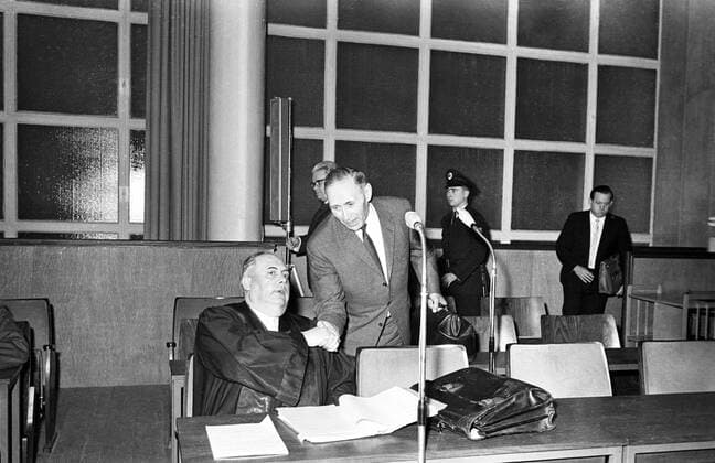 On the trial for war crimes committed at Auschwitz Death Camp , Wilhelm Boger (standing) greets his defence lawyer Dr Rudolf Aschenauer before the start of the session of the Frankfurt Auschwitz trial , which resumed after an on the spot inspection of the former death camp by the judges and others . Boger is one of the 22 defendants charged with the extermination of 2.5 to 4 million persons at the death camp . 21 December 1964 Mono 35mm Transparency !AUFNAHMEDATUM GESCHÄTZT! UnitedArchives1273005