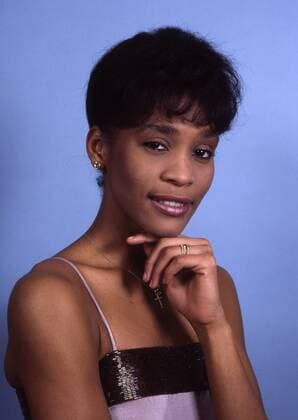 Whitney Houston (Sängerin, Schauspielerin) 03 85 vZ Frau TV Fernsehen Schauspiel Musik Gesang Sängerin Pop USA Amerika seriös dunkelhaarig kurzhaarig dunkelhäutig halb hoch Hand Kinn Schmuck Ohrring Ring lächelnd