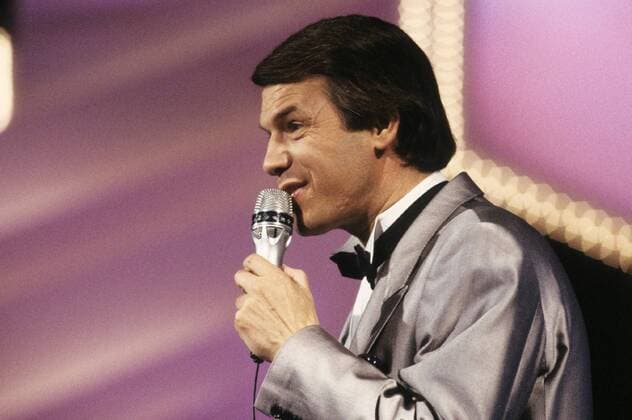 Salvatore Adamo (Sänger) 06 86 dar Salvatore Adamo während der Eröffnungsshow TV-Gala zur Kieler Woche am 25. Juni 1986 Mann Italien Italiener italienisch Sizilien Sizilianer Musik Gesang deutsche Schlager Schlagersänger Schlagerstar dunkelhaarig schwarze Haare kurzhaarig Seitenscheitel seriös festlich feierlich Anzug Jackett weißes Hemd weiß Fliege schwarz stehen stehend neutral singen singend Mikrofon halten haltend in der Hand Auftritt auftreten auftretend Bühne Beleuchtung Bühnenbeleuchtung Scheinwerfer Fernsehen Fernsehsendung Sendung TV TV-Show Show Fernsehstudio Studio Querformat quer Portrait halb