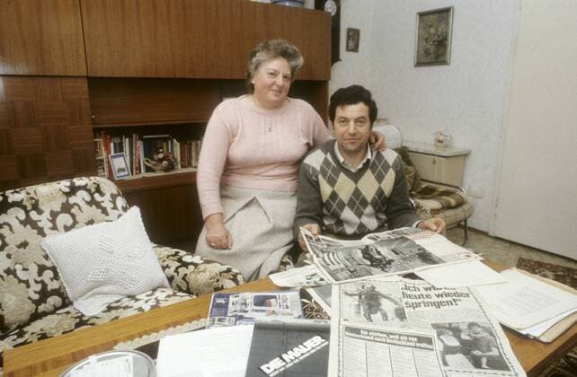 Conrad Schumann mit Ehefrau Gunda 03 86 ru Ex-DDR-Volkspolizist Conrad Schumann mit seiner Frau Gunda zu Hause in Franken im März 1986 mit Zeitungsberichten seiner Flucht vom 15. August 1961 Deutschland deutsch Deutscher Deutsche Mann Einheit deutsche DDR Deutsche Demokratische Republik Hauptstadt geteilt geteilte Stadt Ostberlin Berlin Ost Sozialismus VoPo Mauerflüchtling Flüchtling Soldat Polizist ehemalig ehemaliger geflüchtet Foto historisch historisches Kalter Krieg Mauerbau Flucht am 15. August 1961 german former gdr policeman wall germany quer privat Homestory Wohnzimmer sitzend zeigend Familie exklusiv exklusiver Fototermin