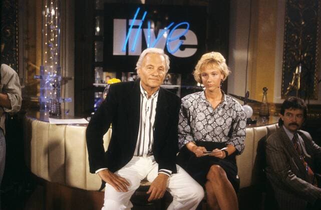 Harry Valerien mit Amelie Fried in live (ZDF) 08 88 - Harry Valerien und Amelie Fried im August 1988 in live (ZDF) german host presenter Talkshow Talk Show Kulisse Dekoration Fernsehstudio Logo Deutschland deutsch Deutscher Mann Fernsehen TV Sport Moderation Sportjournalist Sportjournalismus Journalist Autor Deutsche Frau Moderatorin Autorin Journalistin Journalismus grauhaarig kurzhaarig leger elegant Hemd Jackett blond lockig Rock Bluse quer halb sitzend lächelnd