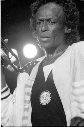 Miles Davis (Jazzmusiker) 08 88 hof Miles Davis im August 1988 auf dem Paris Jazz-Festival Mann Musiker Musik Jazz Jazzmusik dunkelhäutig dunkelhaarig kurzhaarig Locken leger Hemd stehen stehend skeptisch Blick blickend Hand Saal Halle Bühne Scheinwerfer Auftritt Konzert Hochformat hoch Portrait halb sw