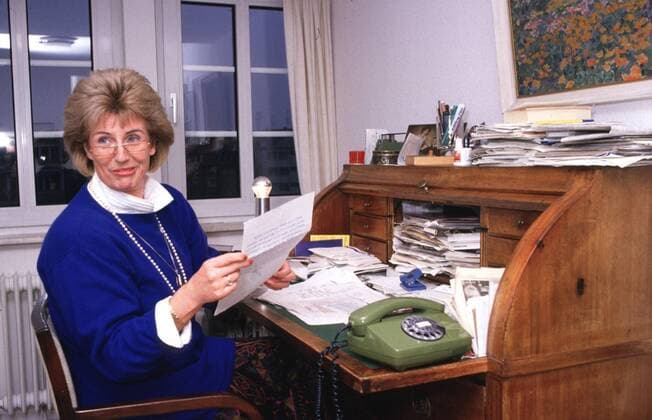 Cornelia Schmalz-Jacobsen (FDP-Politikerin) 11 88 hof Frau Politik FDP Partei blond leger Bluse weiß Pullover blau Schmuck Kette Perlen sitzend Stuhl Wohnzimmer Schreibtisch Sekretär Fenster Lampe Telefon Unterlagen haltend Zettel Brief halb quer lächelnd fragend Brille