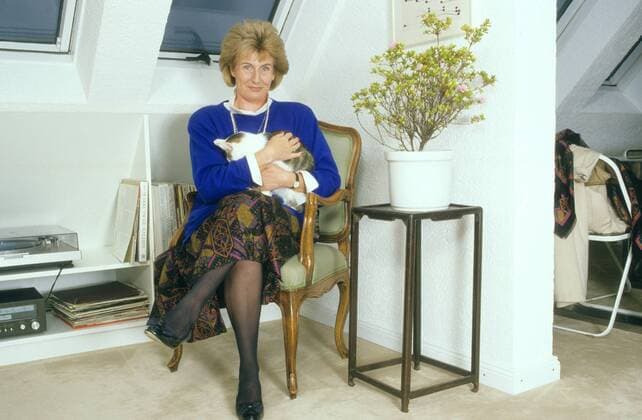 Cornelia Schmalz-Jacobsen (FDP-Politikerin) 11 88 hof Frau Politik FDP Partei blond leger Bluse weiß Pullover blau Rock Kette Perlen Schmuck sitzend Wohnzimmer Stuhl Sessel Fenster Dachfenster Wand Bild Tisch Blume Pflanze Tier haltend Katze ganz quer Beine lächelnd