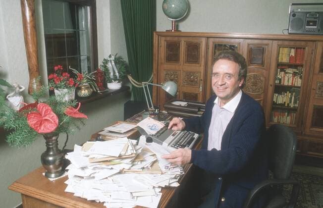 Günter Wewel (Sänger, Moderator) 02 90 hör Günter Wewel im Februar 1990 Deutschland deutsch Deutscher Mann TV Fernsehen Moderation Volksmusik Musik Operette Oper Bass Schlager german singer presenter host quer halb sitzend lächelnd SChreibmaschine Büro Tisch SChreibtisch Fanpost Post Fanbriefe Briefe exklusiv privat Homestory