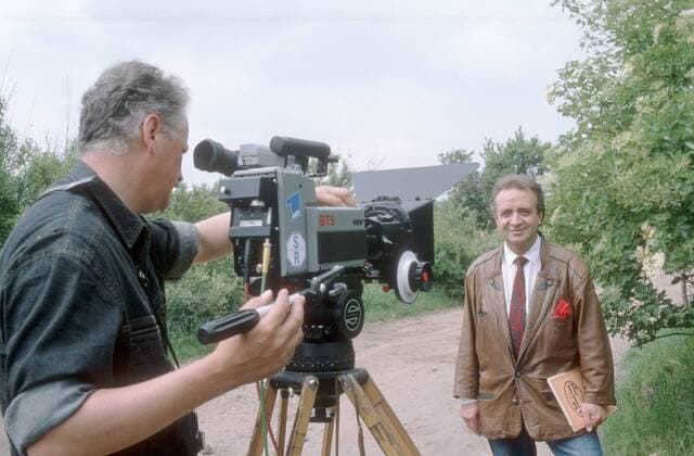 Günter Wewel (Sänger, Moderator) 05 90 hör Günter Wewel in Quedlinburg im Mai 1990 bei Dreharbeiten zu Kein schöner Land Deutschland deutsch Deutscher Mann TV Fernsehen Moderation Volksmusik Musik Operette Oper Bass Schlager Harz DDR german singer presenter host quer halb stehend draußen lächelnd Kamera Fernsehkamera Kameramann exklusiv