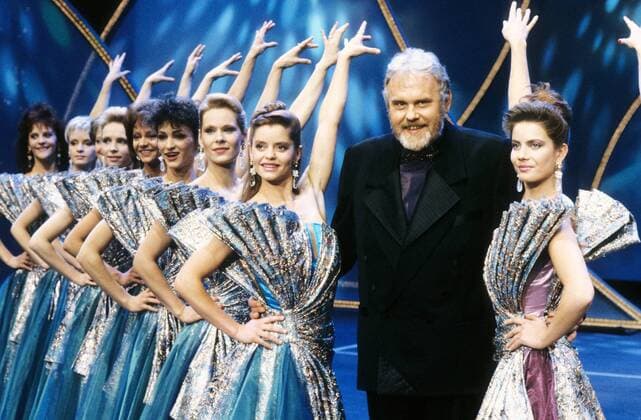 Gunther Emmerlich mit Fernsehballett 02 91 - Mann TV Fernsehen Moderation Moderator Musik Oper Sänger Opernsänger Bass Entertainer grauhaarig kurzhaarig Bart seriös halb quer stehend Bühne Show Kulisse Dekoration Tänzerin Tänzerinnen lächelnd