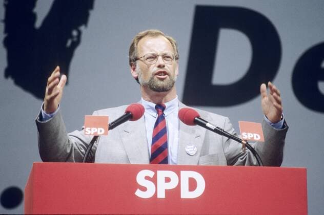 Rudolf Scharping 09 94 mat Mann Politik SPD quer halb sprechend gestikulierend Hand dunkelhaarig Brille Sakko Krawatte seriös Pult Mikrophon Logo Bart
