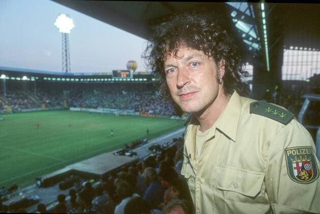 Wolfgang Niedecken in Aus der Rolle fallen (Südwest 3) 08 94 am Mann Musik Pop quer halb stehend neutral dunkelhaarig langhaarig Polizeiuniform Fußballstadion