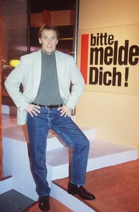 Jörg Wontorra in Bitte melde Dich! (SAT.1) 12 94 kri Mann TV Show Serie Moderation hoch ganz neutral stehend dunkelhaarig Pullover Sakko Jeans leger Logo