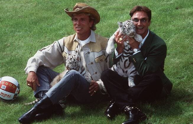 Siegfried (li.) & Roy mit weißen Tigern 07 96 mo Show Magie Entertainment Zauber Tier Tiger haltend sitzend draußen Wiese Ball leger lachend quer ganz