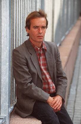 Martin Amis (Schriftsteller) 10 96 am Mann Literatur Schriftstellerei Autor England dunkelhaarig leger HEMD kariert Jackett draußen Hände sitzend Mauer neutral halb hoch
