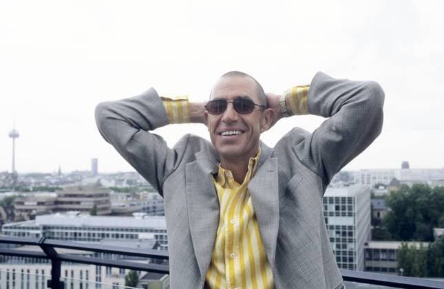 Stephan Remmler (Musiker, Sänger) 09 96 mal Musik Pop Gesang Mann dunkelhaarig kurzhaarig Sonnenbrille Schmuck Ohrring leger Hemd gestreift Jackett draußen stehend Gebäude Stadtansicht Geländer Hand posierend quer halb