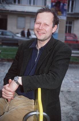 Axel Milberg (Schauspieler) 03 97 kück Mann TV Fernsehen Schauspiel dunkelhaarig leger Hemd Jacke Dreitagebart draußen sitzend aufstützend Geländer Haus Gebäude lächelnd halb hoch Hände