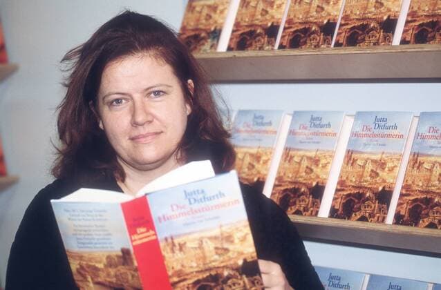 Jutta Ditfurth (Autorin) 10 98 am Frau Politik Autor Journalismus Literatur Schriftstellerei Buch leger Pullover langhaarig dunkelhaarig neutral Titel Logo Die Himmelsstürmerin halb quer stehend haltend Bücherregal