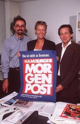 v.li.: Eric Markuse, Marion Horn, Hansjörn Muder 06 99 her Journalismus Publizistik Zeitung Zeitschrift Redaktion Büro Zimmer Tisch Hamburger Morgenpost Regal Bücherregal stehend haltend Plakat Logo Schild lächelnd halb hoch