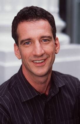 Heio von Stetten (Schauspieler) 07 99 her Mann TV Fernsehen Schauspiel Film dunkelhaarig leger Hemd grau gestreift sitzend Portrait hoch lächelnd Säule weiß
