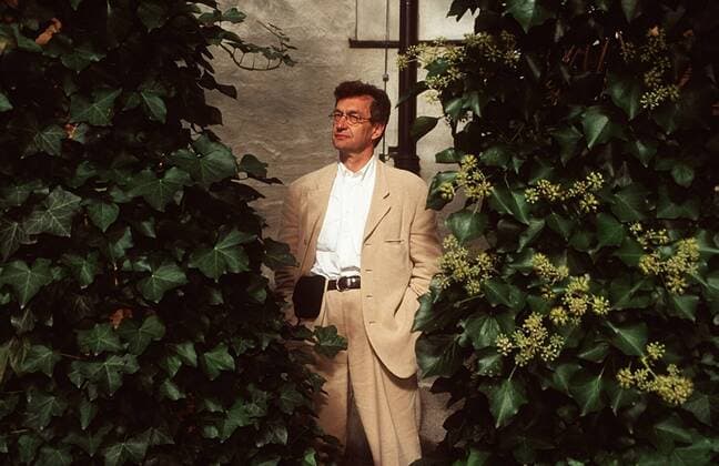 Wim Wenders, 75. Geburtstag am 14. August Wim Wenders (Regisseur) 10 99 bla Mann TV Fernsehen Film Regie dunkelhaarig Brille leger Anzug Jackett beige Hemd weiß Schnürstiefel stehend draußen Hof Garten Park Haus Gebäude Wand Pflanze Efeu halb quer Hände in den Taschen nachdenklich ernst Gürteltasche