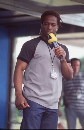 Mola Adebisi in Interaktiv on road 2000 (VIVA) 06 00 thg Mann TV-Moderator Moderation TV Fernsehen Musik-Sender Musiksender dunkelhäutig dunkelhaarig langhaarig Zöpfe Rastazöpfe leger T-Shirt bunt Hose Jeans Kette Band um den Hals mit Karte Ausweis stehend draussen auf Bühne halb hoch Mikrophon haltend sprechend moderierend Fototermin VIVA-Teenie-Tag im Safaripark Stukenbrock am 05.06.2000