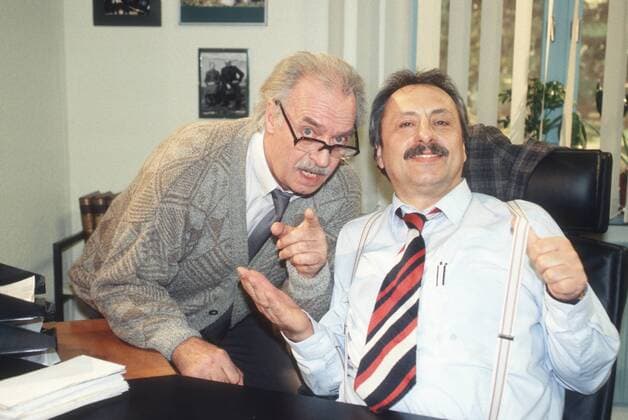 Wolfgang Stumph (re.) und Achim Wolff in Salto Kommunale (ZDF) 12 00 ker Mann Schauspieler Schauspiel TV Fernsehen Serie Film Komik grauhaarig kurzhaarig Schnäuzer leger Raum Zimmer Büro Amt Behörde Tisch Schreibtisch halb quer Szene Fototermin Salto Kommunale (Comedy-Serie, ZDF)