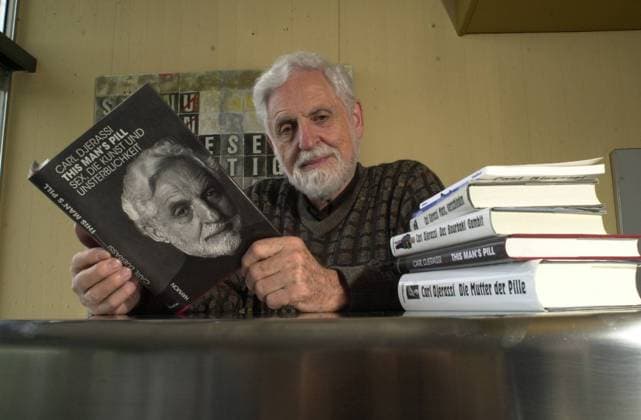 Carl Djerassi (Chemiker Autor) 06 01 teu Mann Österreich Chemie Wissenschaft Forschung Wissenschaftler Forscher Erfinder Entdecker der Pille Anti-Baby-Pille hormonelle Empfängnisverhütung Verhütung Literatur Kunstmäzen Romancier grauhaarig Bart leger Pullover quer halb lächelnd Tisch sitzend Buch This Man s Pill Bücher lesend Auftrag WB e-mail