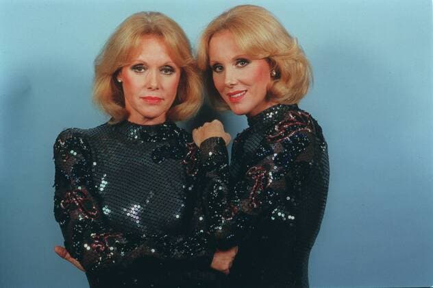 Alice und Ellen Kessler (Showstars) 10 84 vZ Frau Frauen Kessler-Zwillinge Zwilling Showstars Sängerinnen Sängerin Gesang Musik Duo Entertainerinnen Entertainerin Entertainment Schauspielerinnen Schauspielerin Schauspiel Theater TV Fernsehen blondiert blond Schmuck Ohrring leger Kleid blau glitzernd Pailletten eng stehend Studio vor Wand hellblau halb quer lächelnd posierend angelehnt umarmend Farbnegativ Internegativ von Bild Nummer 510555