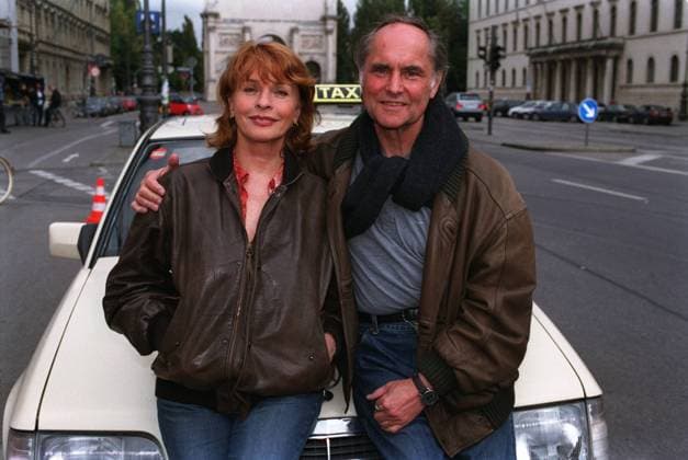 Die schnelle Gerdi (ZDF), Hauptdarstellerin Senta Berger mit Ehemann und Regisseur Michael Verhoeven 09 02 gra TV Fernsehen Produktion Film Serie Schauspiel Schauspielerin Darstellerin Hauptdarstellerin Senta Berger Regie Regisseur Michael Verhoven Ehepaar Außenaufnahme draußen Straße Platz leger stehend sitzend Motorhaube Auto Wagen PKW Taxi halb quer lächelnd posierend angelehnt umarmend Fototermin Die schnelle Gerdi und die Hauptstadt am 02.09.2002 in München Foto: Nicolas Gradicsky