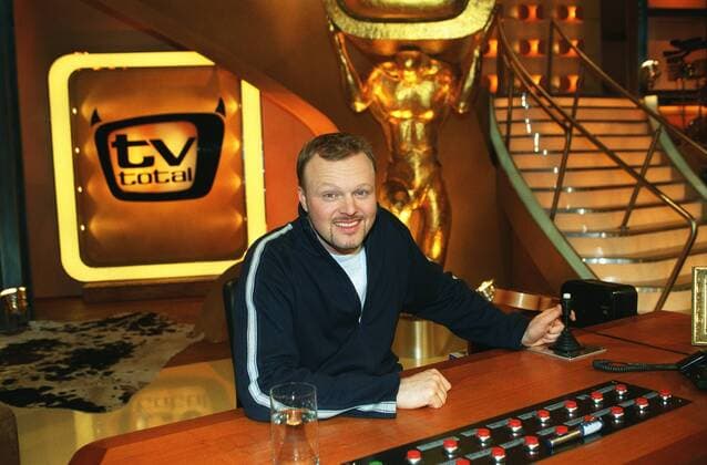 Stefan Raab in tv total (ProSieben) 01 03 pp Mann Moderator TV Fernsehen Moderation Musiker Musik Pop Gesang Sänger Produktion Unterhaltung Show dunkelhaarig kurzhaarig leger Trainingsjacke Sportjacke Shirt sitzend TV-Studio Kulisse Dekoration Logo halb quer sitzend lächelnd Tisch Moderationstisch Pult Glas Wasserglas Fototermin tv total (ProSieben) am 06.01.2003 in Köln