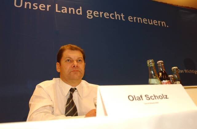 Olaf Scholz (Politiker) 02 04 wow Mann Politik Politiker Partei SPD Generalsekretär Rücktritt Bekanntgabe Ankündigung angekündigt am 6. Februar 2004 dunkelhaarig kurzhaarig leger Hemd Krawatte halb quer sitzend lächelnd Podium Namensschild Schild Name Slogan Unser Land gerecht erneuern Fototermin am 05.02.2004 in Gütersloh