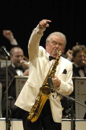 Max Greger 01 06 thg Max Greger im Kuppelsaal des HCC Hannover am 19.01.2006 im Rahmen eines Konzertes der Swinglegenden Kuppel Konzertsaal Konzerthaus Konzerthalle Auftritt Gesangsgruppe Gruppe Veranstaltung Gesang Swing Jazz Jazzmusik Musik Sänger Tanzmusik Schlager Strasser Greger Kuhn SWR-Big Band Big Band Musiker Bühne Mann weißhaarig kurzhaarig Mikro Mikrofon weißer Smoking weiß Hemd Fliege Einstecktuch elegant seriös festlich Instrument Musikinstrument Blasinstrument Blechbläser Saxophon Saxofon haltend spielend blasend einen Arm schwingend Geste Gestik gestikulierend hoch Hochformat halb