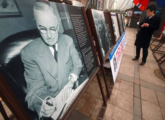 Koreans walk past a sidewalk exhibition of the Korean war, including a photo of American President Harry Truman signing the National Emergency Declaration when Communist China invaded Korea, in Seoul on January 31, 2013. The Korean War cost more than $50 billion and 33,000 U.S. lives, plus another 110,000 were wounded.  ICN2013013110