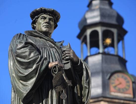 Denkmal des Reformators Martin Luther auf dem Marktplatz in Eisleben (Sachsen-Anhalt) mit dem Turm der St. Andreaskirche im Hintergrund am 23.9.2009. Das Denmal, das 1883 von dem Berliner Bildhauer Rudolf Siemerin errichtet wurde, zeigt Luther, wie er die Bannbulle des Papstes zerreißt. In Eisleben wurde der Reformator am 10.11.1483 geboren; am 18.2.1546 starb er hier. In der Andreaskirche hielt er seine letzten Predigten. Der Überlieferung nach schlug Martin Luther am 31. Oktober 1517 seine 95 Thesen gegen den Ablasshandel der Kirche an die Tür der Wittenberger Schlosskirche. Das Ereignis gilt als Beginn der Kirchenreformation. Der 31. Oktober wird deshalb von evangelischen Christen als Reformationstag gefeiert. 2017 jährt sich der legendäre Thesenanschlag Martin Luthers an der Schlosskirche zum 500. Mal. Reformationstag am 31. Oktober 325831 EDITORIAL USE ONLY
