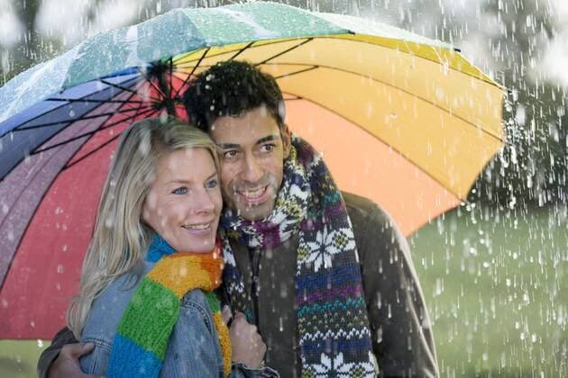 Lächelndes Paar unter regenbogenfarbenem Schirm genießt den Regen iblhfm03011355.jpg