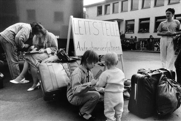Seit Ende Mai 1989 ist das für 500 DDR Übersiedler ausgelegte Zentrale Aufnahmelager Hessen (ZAH) in Gießen mit etwa 1000 Menschen belegt. Weitere tausend Menschen müssen in Turnhallen und einem evangelischen Gemeindezentrum übernachten. Foto: Angekommene Übersiedler füllen neben dem Behelfsbüro, einem Unimog des Technischen Hilfswerks, ihre Aufnahmeformalitäten aus. DER ABDRUCK DES EPD-FOTOS IST HONORARPFLICHTIG! Seit Ende Mai 1989 ist das für 500 4110 EDITORIAL USE ONLY