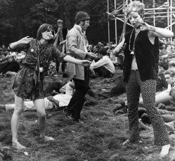 Flower Power at Woburn Abbey unidentifed british flower children dressed in a array of garments with floral offerings and painted bodies and faces in the grounds of Woburn Abbey Bedford on the second day of a three day Love In 1967 a mini skirted girl holds a flower in her mouth another has a bell attacted to a string of beads around her neck with bell bottomed trousers and bare midriff as they dance in the field UnitedArchives00934115 