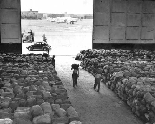 70 Jahre Berliner Luftbrücke am 26. Juni Beginn der Berlinblockade, 70. Jahrestag am 24. Juni Fassburg, British Zone: German workers carry sacks of coal from a hangar dump to waiting Dakotas on the tarmac of this airfield in the British sector of Germany, for transport to Berlin. The Royal Air Force, having sufficiently stocked besieged Berlin with food, is now following the Americans in dumping tons of coal into the city to relieve the fuel and power shortage caused by the Soviet blockade. Dakotas, carrying 7,500 pounds of coal in white sacks or kitbags, took off at the rate of seven per hour for Gatow (Berlin) airfield. 20th July 1948  UnitedArchives01025113