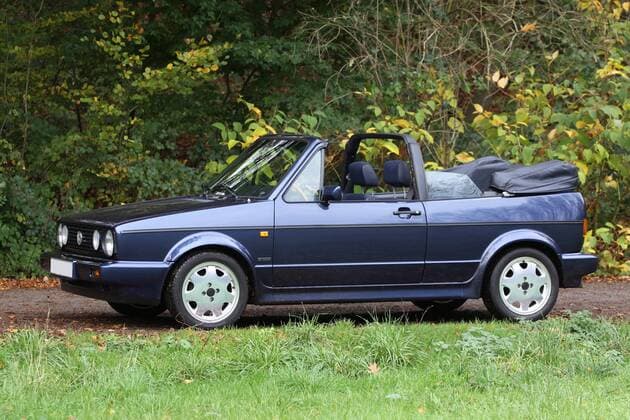 VW Golf 1 Cabriolet Quartett (Baujahr 1993, 98 PS, Farbe: Inkablau Metallic, Youngtimer) mit geöffnetem Verdeck im Herbst im Wald.
