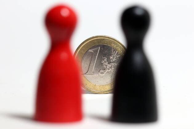 Spielfiguren Mensch aergere dich nicht in den Farben schwarz und rot stehen hinter einer Euro Geldmuenze