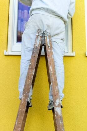 Ein Maler auf einer Stehleiter. Hausfassade wird gestrichen. Renovieren und sanieren McPBBO McPBBO